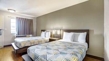 A hotel room with two beds, a window with curtains, a bedside table, and a wall-mounted light fixture.