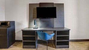 A modern room with a flat-screen TV mounted on a wooden wall, a desk with a blue chair, and a microwave on a cabinet. - Motel 6 Amarillo, TX - Airport (Amarillo)