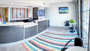 A modern reception area with a large number '6' sign, a flat-screen TV, and a colorful striped carpet. - Motel 6 Amarillo, TX - Airport (Amarillo)