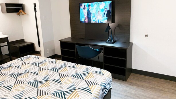 A hotel room with a bed, a desk, a chair, a TV, and a wardrobe. - Motel 6 Amarillo, TX - Airport (Amarillo)
