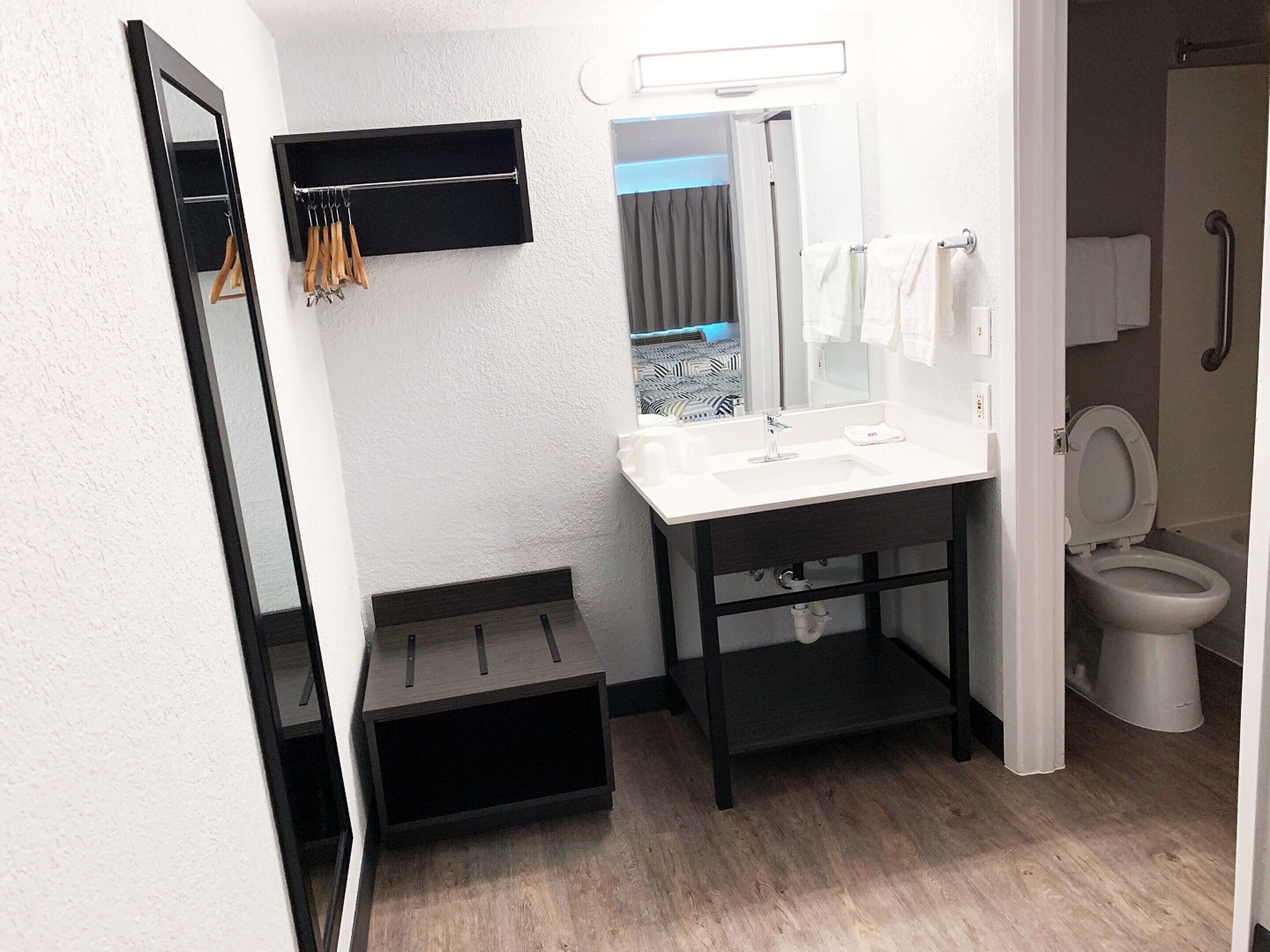 A modern bathroom with a white sink, mirror, and toilet. There is a towel rack above the sink and a shelf below it.