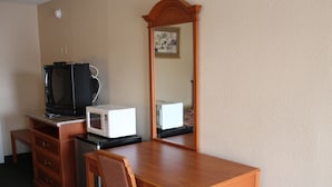 A hotel room with a wooden desk, a microwave, a television, and a chair.