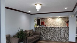A living room with a sofa, a potted plant, and a kitchen area with a stone backsplash.