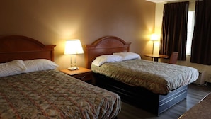 A hotel room with two beds, each with a wooden headboard, a bedside table with a lamp, and a small table with a chair.