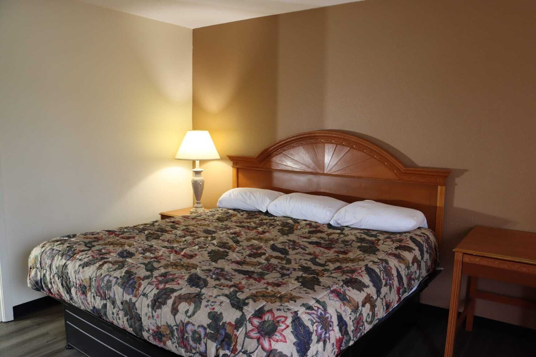 A hotel room with a bed, a nightstand with a lamp, and a wooden nightstand.