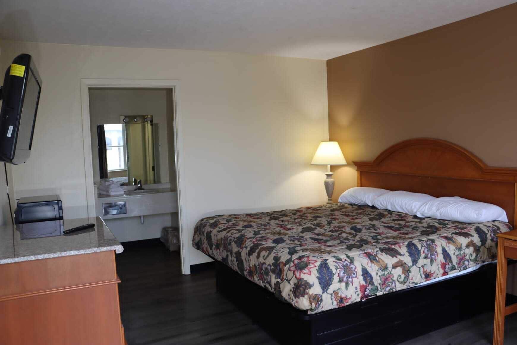 Een hotelkamer met een bed, een bureau, een spiegel, een lamp en een televisie.