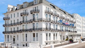 Un hôtel à plusieurs étages, doté de balcons, d’une entrée couverte et de drapeaux.
