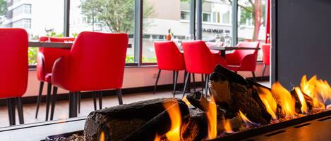 A restaurant interior with a fireplace, red chairs, and a view of the outside.
