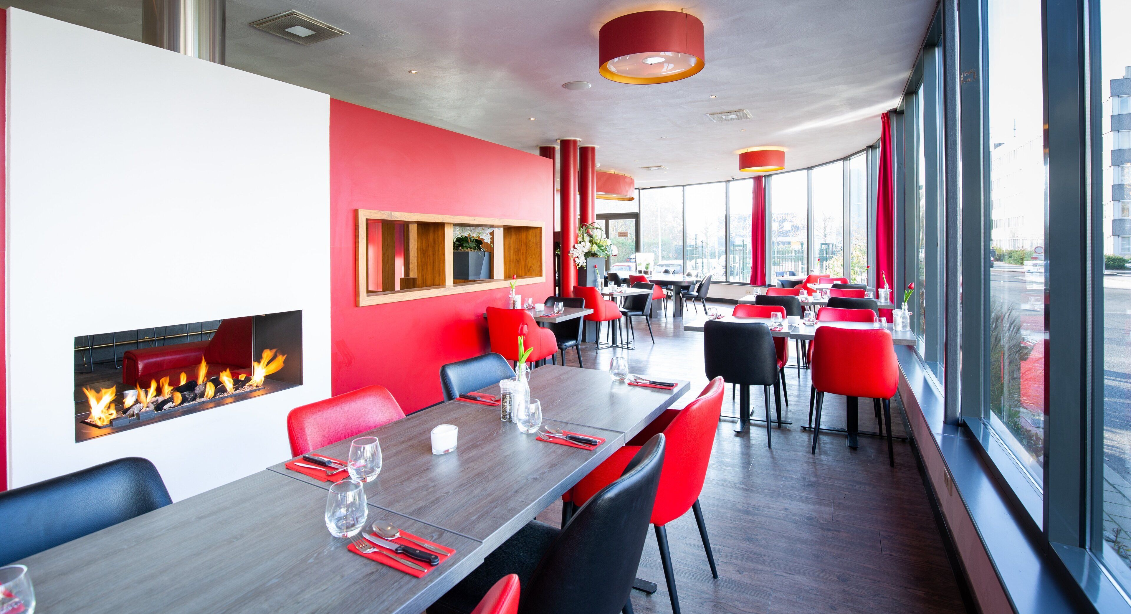 Un restaurante moderno con sillas rojas y negras, una larga mesa de comedor y una chimenea.