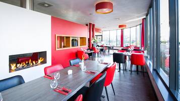 Un restaurante moderno con sillas rojas y negras, una larga mesa de comedor y una chimenea.