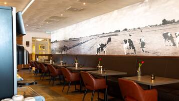 A restaurant with booths, tables, and chairs. There is a wall mural of cows in a field.