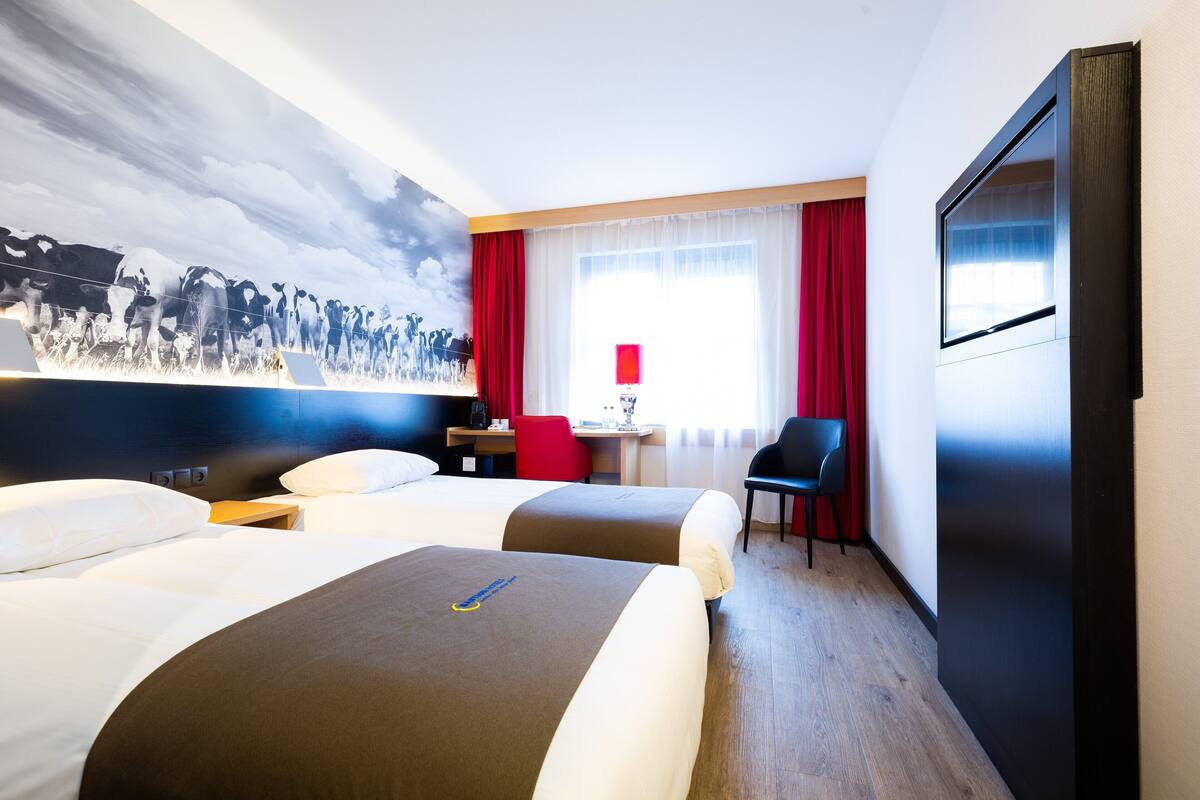 Hotelkamer met twee bedden, een bureau, een stoel, een televisie en een groot muurschildering.