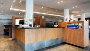 A reception area with a wooden counter, a digital screen, and a view of the water. - Bastion Hotel Den Haag Rijswijk (Rijswijk)