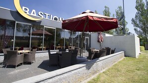 A restaurant with outdoor seating, a large crescent sign, and a red umbrella. - Bastion Hotel Schiphol Hoofddorp (Hoofddorp)