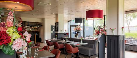 A restaurant with wooden flooring, red and black chairs, and tables set with red napkins and clear glasses.