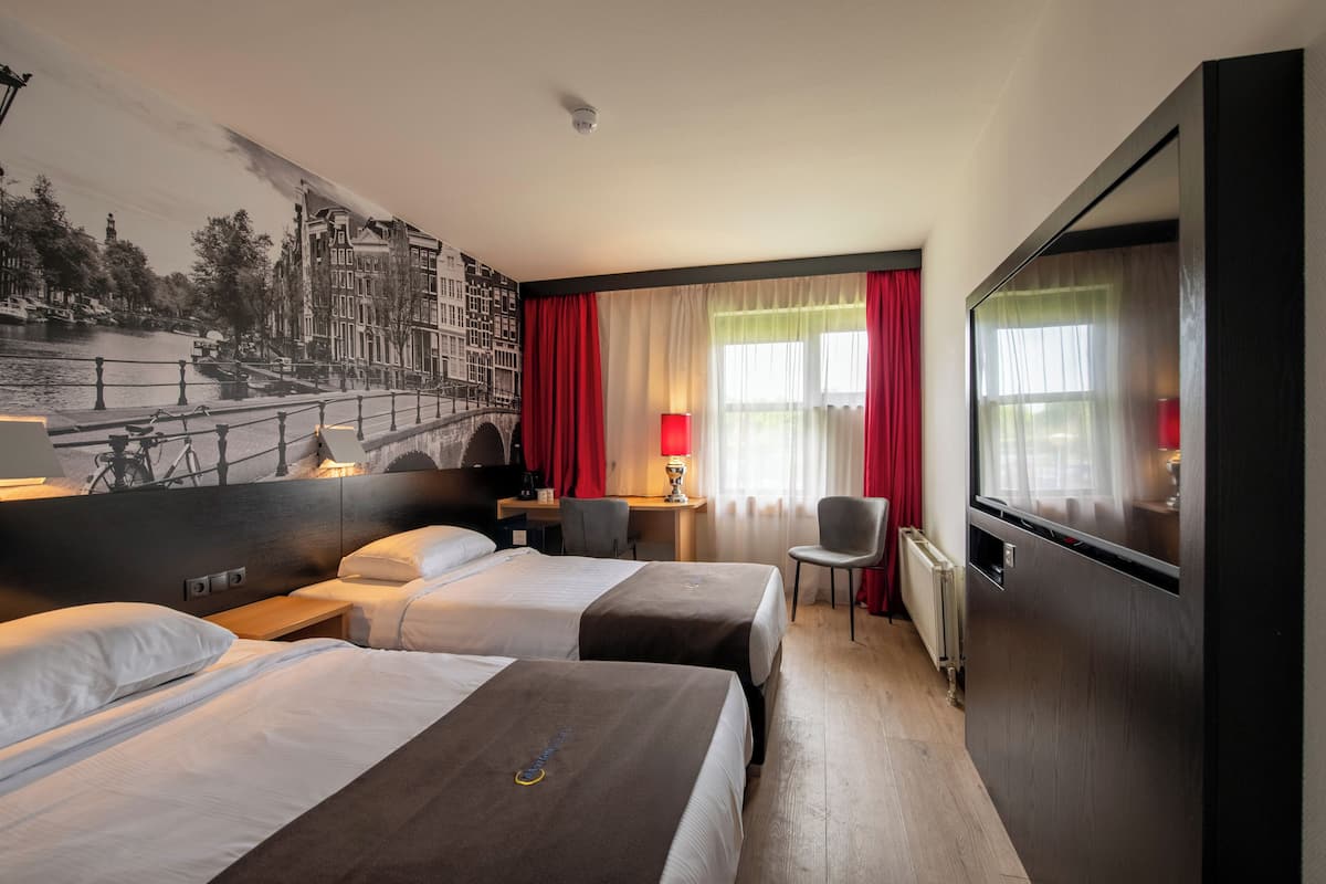 Hotelkamer met twee bedden, een bureau, een stoel, een televisie en een groot raam met rode gordijnen.