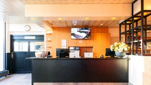 A reception area with a black counter, a clock, a television, and a flower arrangement. - Bastion Hotel Schiphol Hoofddorp (Hoofddorp)