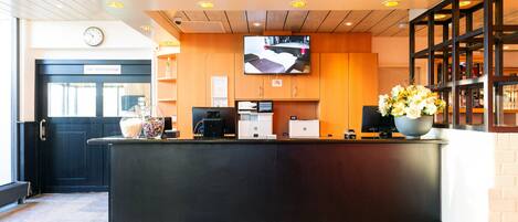 Una zona de recepción con un mostrador negro, un reloj, un televisor y un arreglo floral.