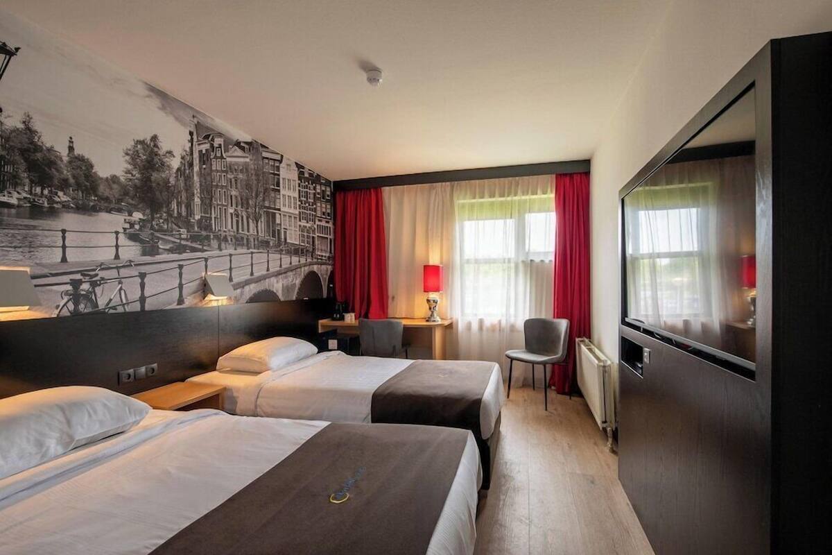Een hotelkamer met twee bedden, een bureau, een stoel, een televisie en een muurschildering van een stadsgezicht.