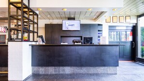 Un espace d’accueil avec un comptoir sombre, un téléviseur fixé au mur et des certificats encadrés accrochés au mur.