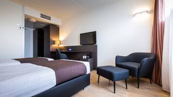 A hotel room with a bed, a desk with a computer, a chair, and a TV on the wall.