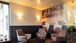 Un hall d’hôtel moderne avec trois fauteuils, une table basse noire et une grande fresque murale.