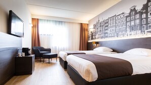 Une chambre d’hôtel avec deux lits, un téléviseur à écran plat, un bureau avec une chaise et une grande fresque murale représentant un paysage urbain.
