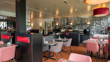 A modern restaurant with wooden flooring, red accents, and a mural of a cityscape.