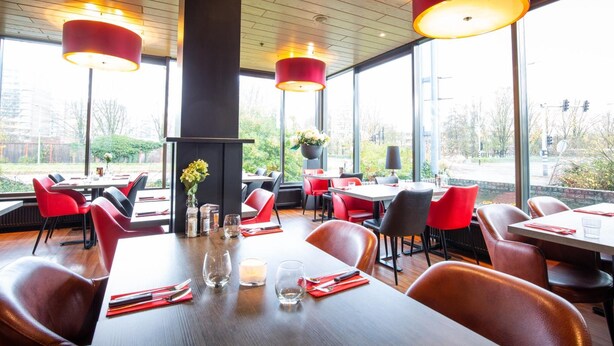 Un restaurant avec des chaises et des tables rouges, de grandes fenêtres et des lampes suspendues rouges.