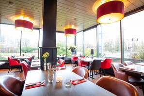 Un restaurant avec des chaises et des tables rouges, de grandes fenêtres et des lampes suspendues rouges.