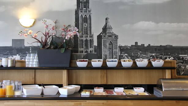 A breakfast buffet with various food items and a potted plant. - Bastion Hotel Utrecht (Utrecht)