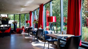 Een modern restaurant met rode gordijnen, grote ramen en zwarte stoelen.