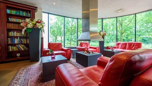 A modern living room with red leather sofas, a fireplace, and a large bookshelf filled with books. - Bastion Hotel Utrecht (Utrecht)