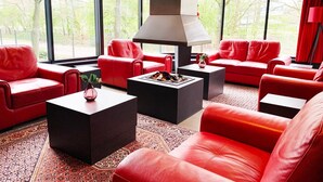 A modern living room with red leather sofas, black coffee tables, and a large fireplace. - Bastion Hotel Utrecht (Utrecht)