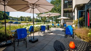 An outdoor patio area with tables and chairs, some covered by umbrellas, and a building in the background. - Bastion Hotel Utrecht (Utrecht)