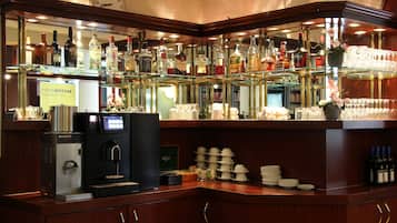 Een bar met een koffieapparaat, flessen drank op planken en een stapel witte bekers.