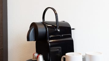 A black coffee maker with a handle, two white mugs with logos, and a dark wooden surface.