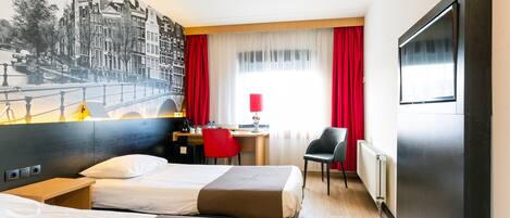 Habitación de hotel con dos camas, un escritorio, una silla, un televisor y un mural de un paisaje urbano.