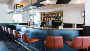 A bar area with a counter, bar stools, and a shelf with bottles. - Bastion Hotel Amsterdam Amstel (Amsterdam-Duivendrecht)