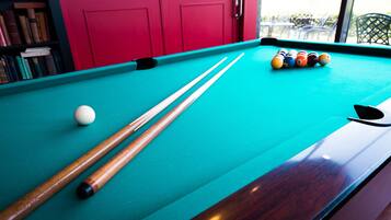 A pool table with a green felt surface, two pool cues, and a set of billiard balls.