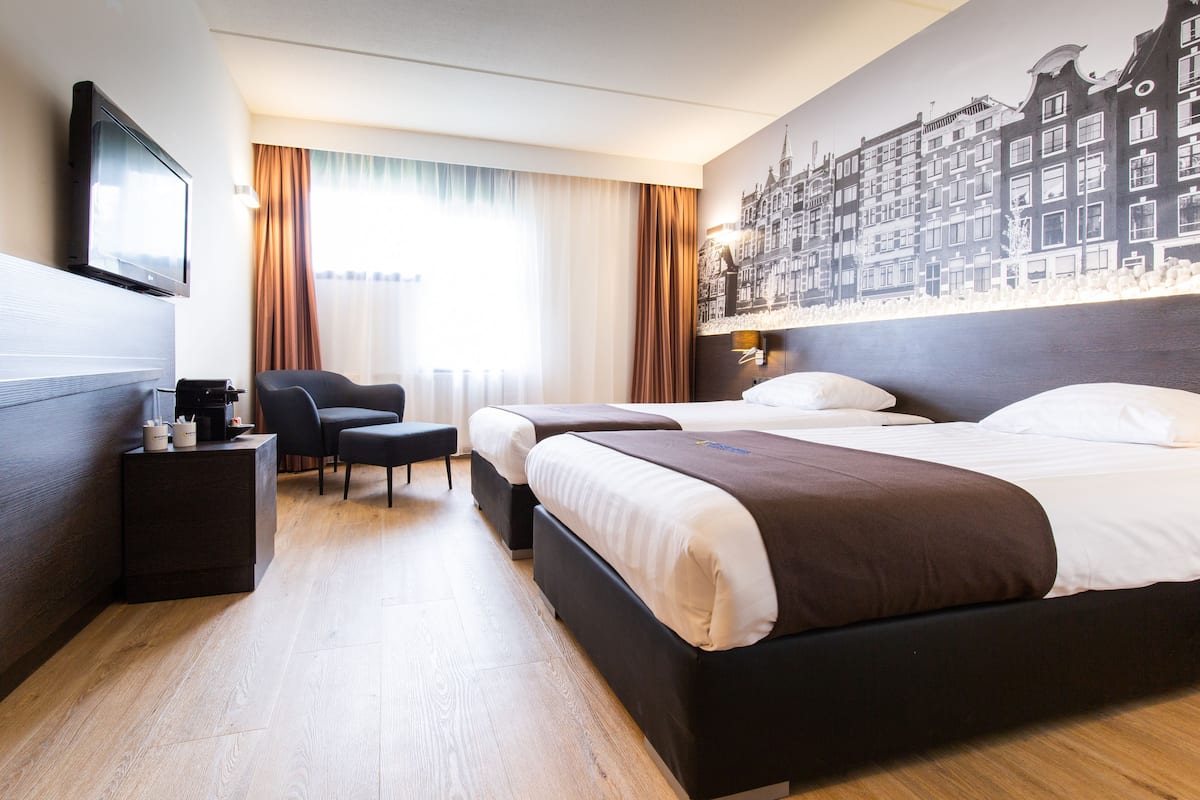 A hotel room with two beds, a flat-screen TV, a desk with a chair, and a large cityscape mural on the wall.