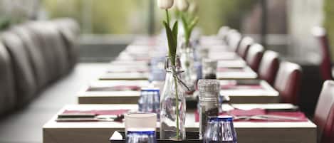 A dining table set with red napkins, clear glassware, and a single white tulip in a glass vase.