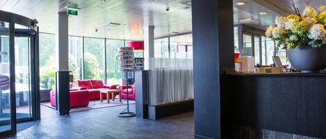 A modern lobby with a reception desk, red seating area, and a large potted plant.