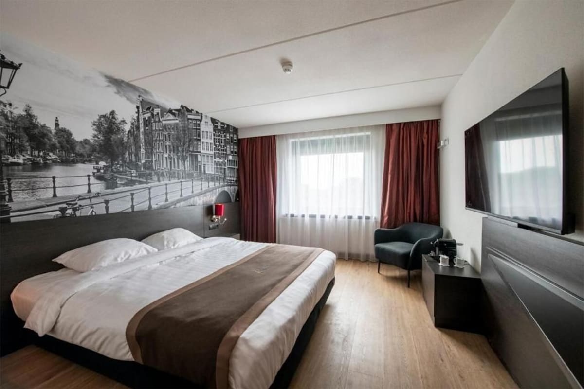 Une chambre d’hôtel avec un grand lit, un bureau, une chaise, une télévision et une fresque murale.