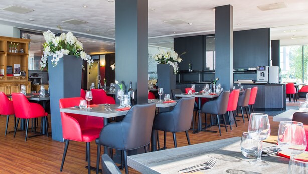 A restaurant with red and grey chairs, wooden tables, and a bar area. - Best Western Plus Amsterdam Airport Hotel (Hoofddorp)
