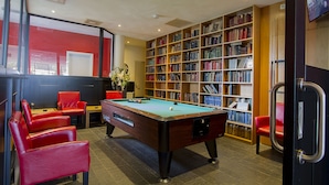 Une table de billard, des chaises rouges, une bibliothèque et un téléviseur dans une pièce dont un mur est rouge et qui est dotée d’étagères en bois.