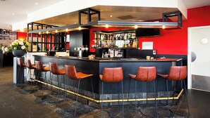 Un espace bar avec un comptoir noir, des murs rouges et des tabourets de bar marron.