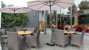 Terraza con sillas de mimbre y sombrillas grandes, pared de vidrio y vista al área de comedor interior.
