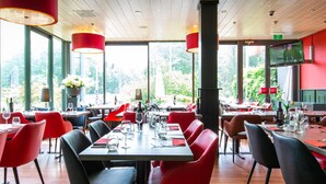 Un restaurante con sillas rojas, mesas de madera y grandes ventanales que dan a zonas verdes.
