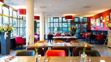 A restaurant with large windows, red and black chairs, and tables set for dining.